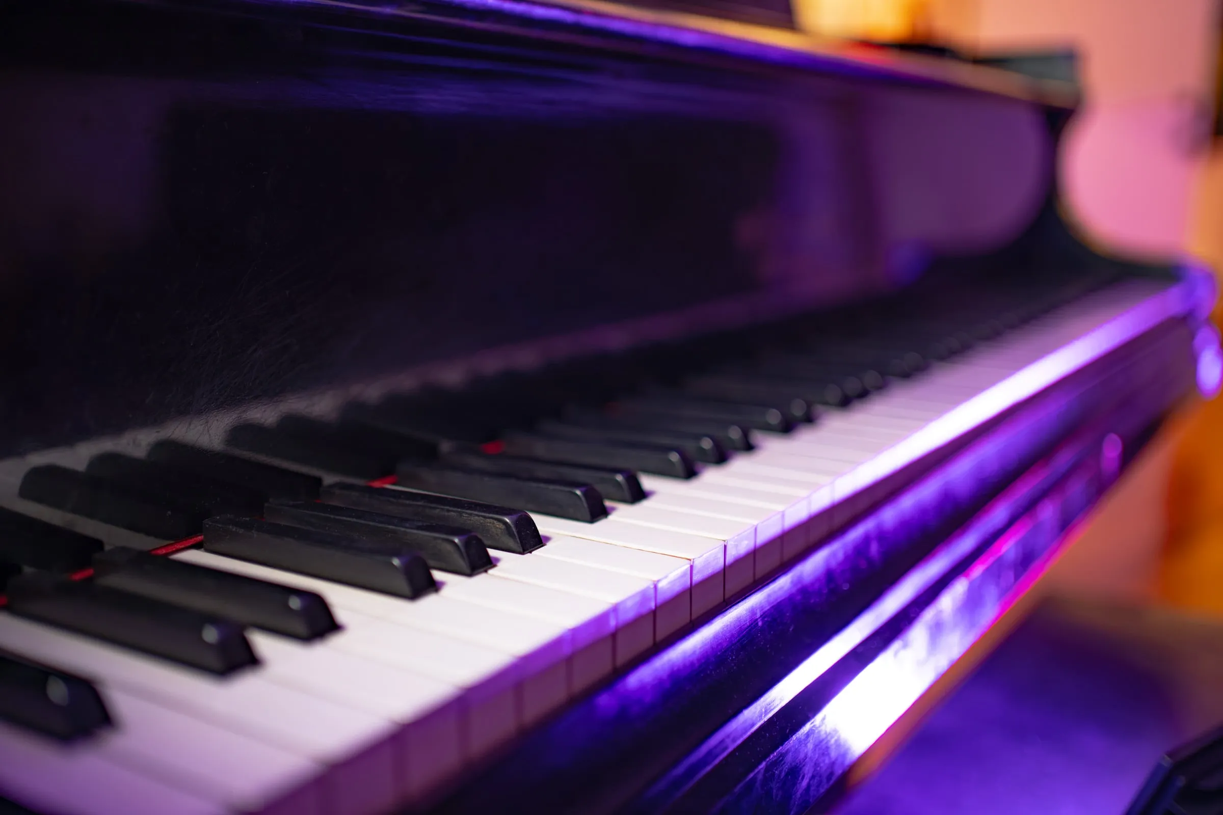 The grand piano up close, purple light across the keys.