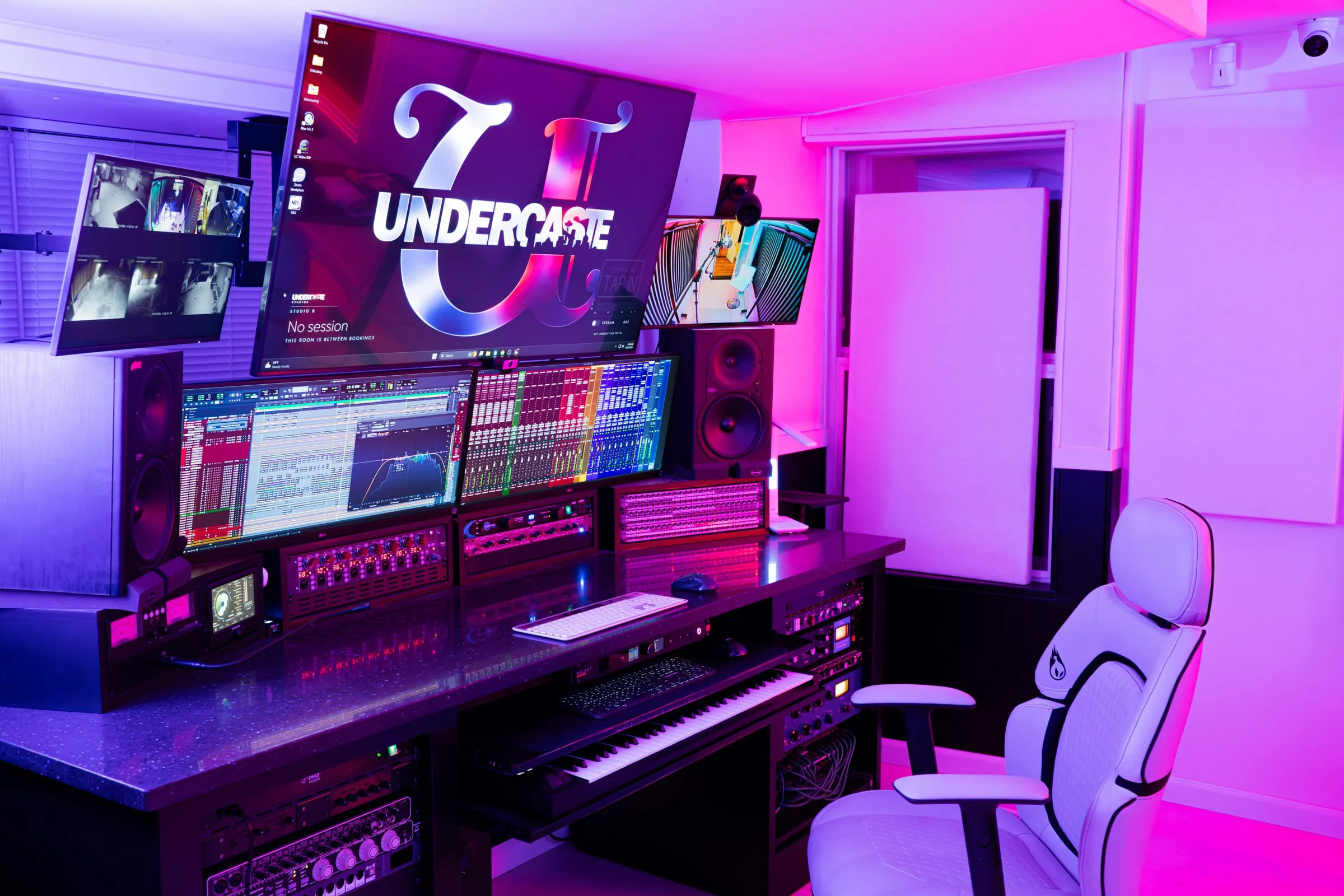 Studio B lit pink and blue: the session on the screens, racks under the desk, chair pulled up.